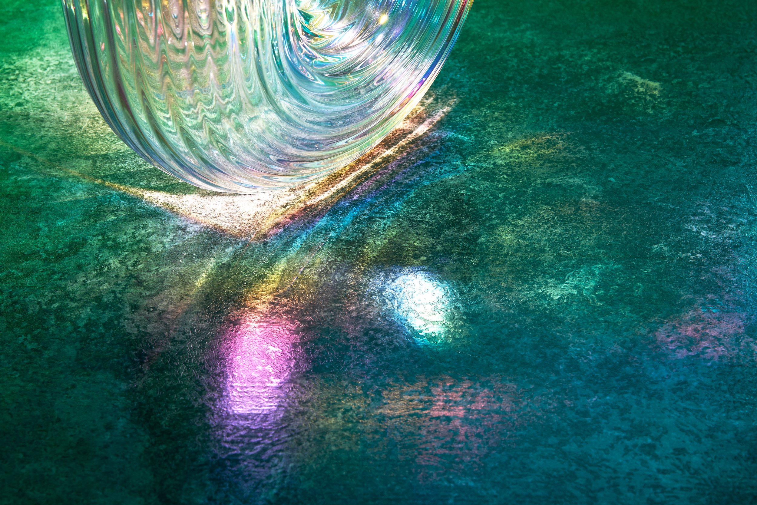 Transparent arched glass sculpture resting on stone in emerald light